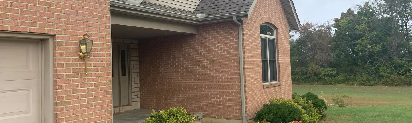 The front of the house in 2019, brick running from the garage gable past the covered entrance to a gabled wing