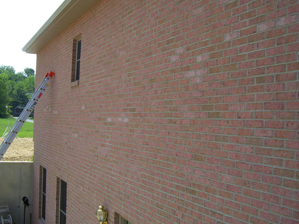 The side elevation in 2007 with an extension ladder rigged against it, light units still showing in the brick above a walkout lower level and freshly strawed ground