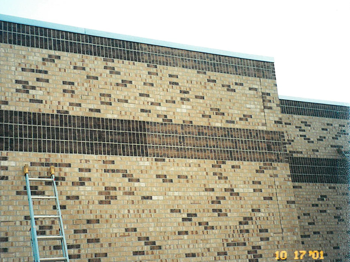 The upper wall of the school in 2001 with two dark soldier bands running across it and an aluminium ladder standing against the buff brick below