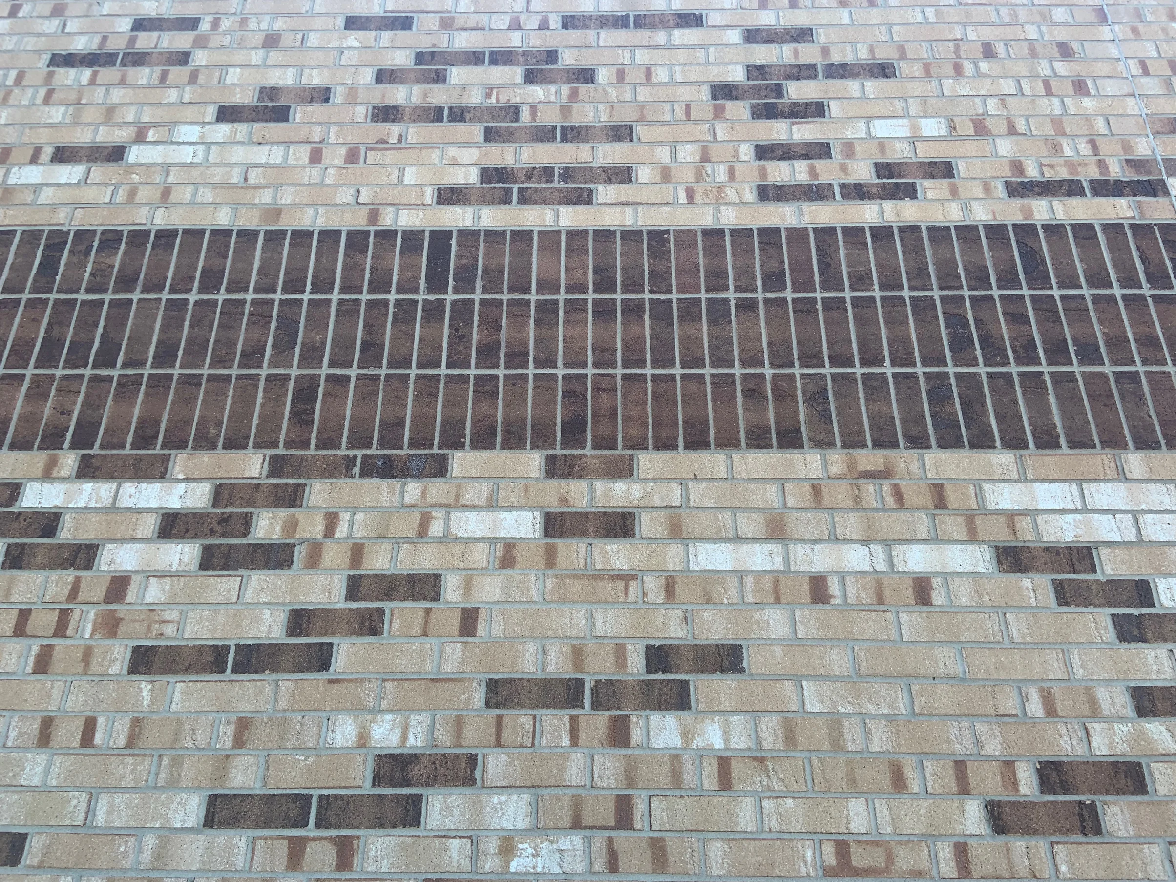 Close view of the dark band in 2019, its upright units reading as one dark brown range against the buff and cream brick above and below