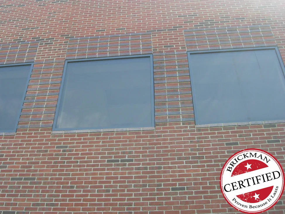 The college wall from below in 2019, a curving roofline over three tall windows and the brick reading as one even red range from the sills to the parapet.