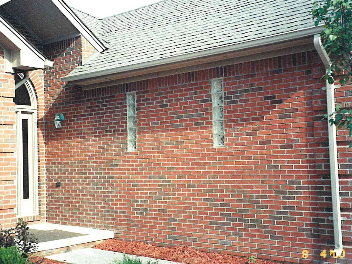 The side wall of the house in 2000 with the work finished, an even red and brown range running past two glass block windows to the arched entry