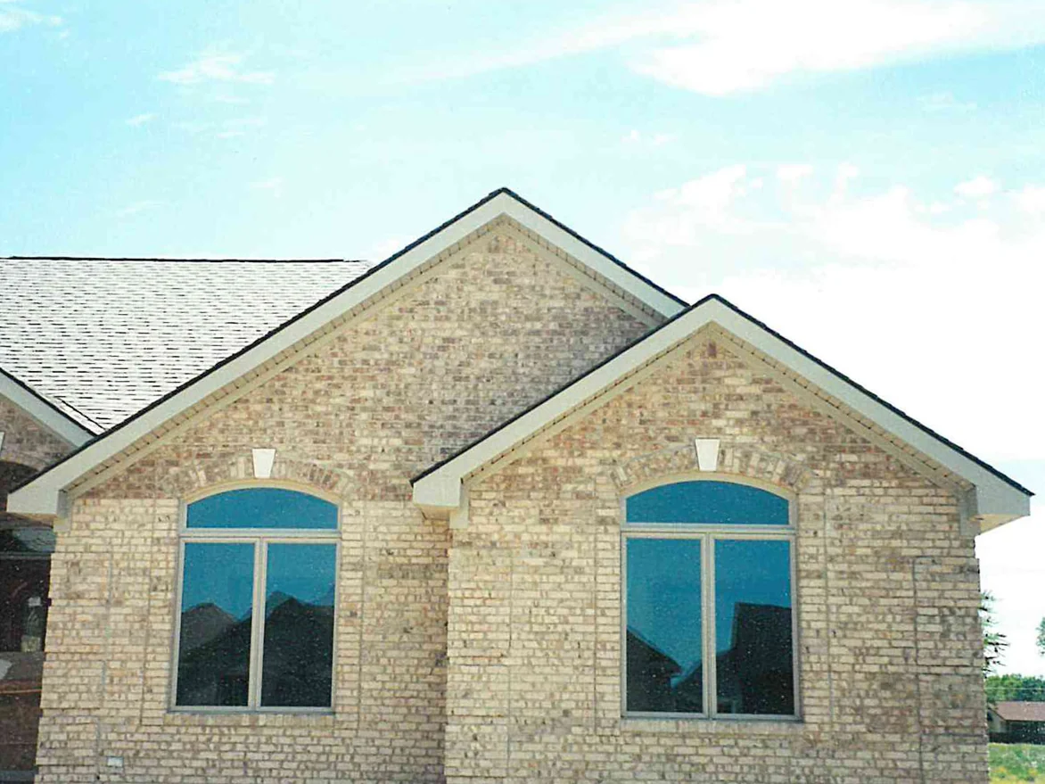 Two brick gables with arched windows on a newly built single-story house, the brick a pale cream and tan mix