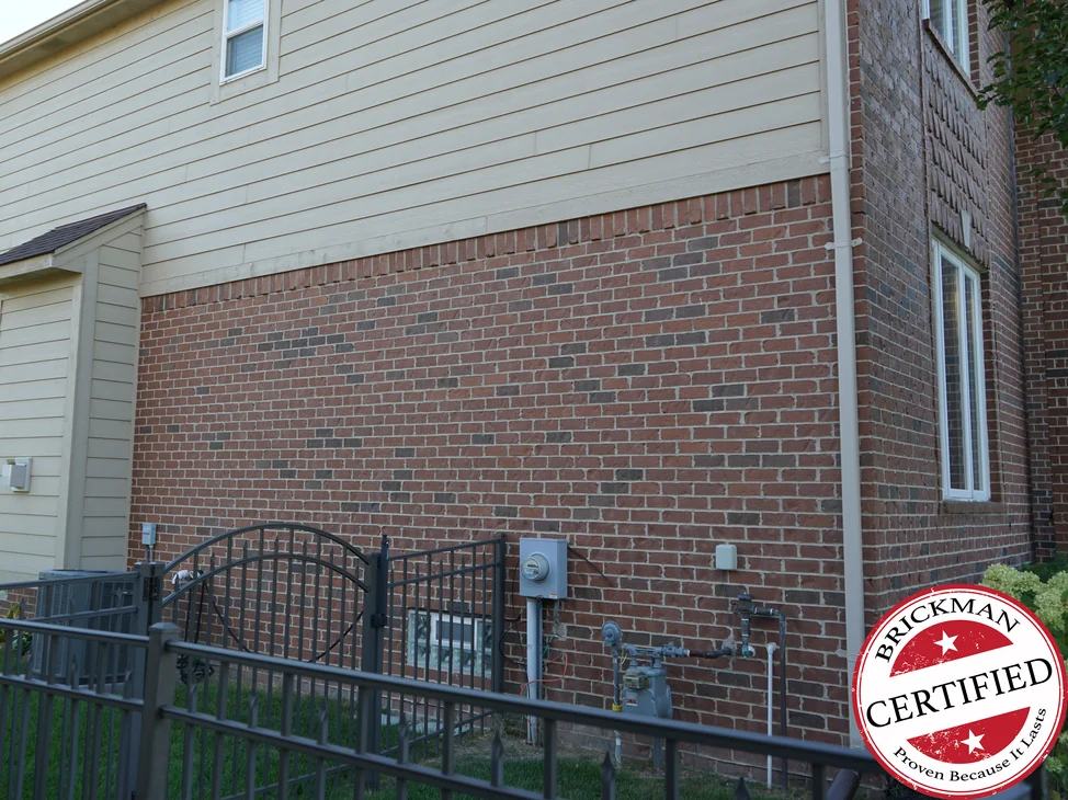 The side elevation of the Macomb house in 2019, its red brick reading as one range under cream lap siding.