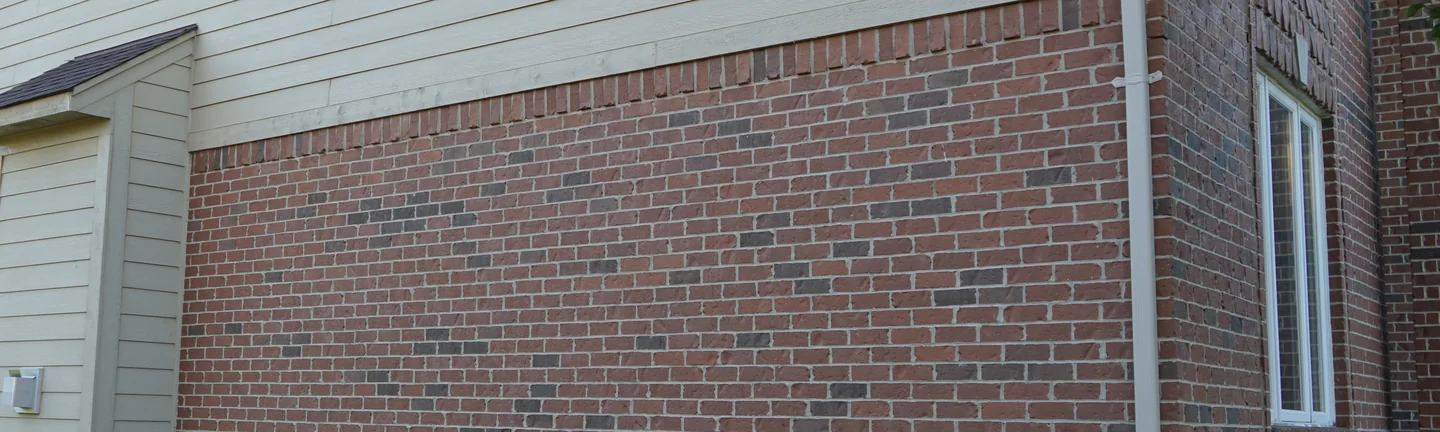 The brick flank of the Macomb house in 2019, its red units reading as one range under cream lap siding