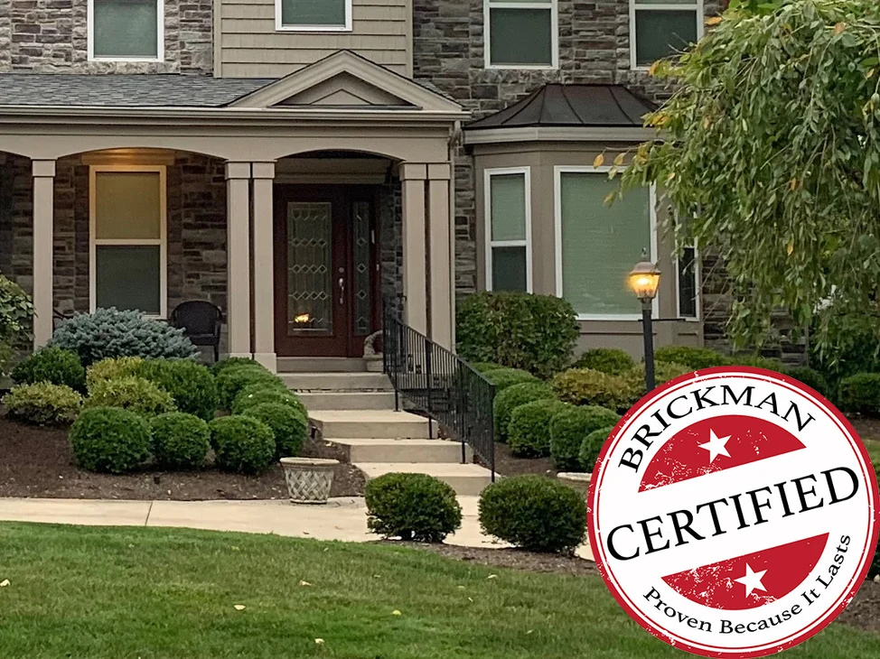 The porch and front door of the manufactured stone house in 2020, grey window sills inside the stone blend, with the certification stamp in the corner