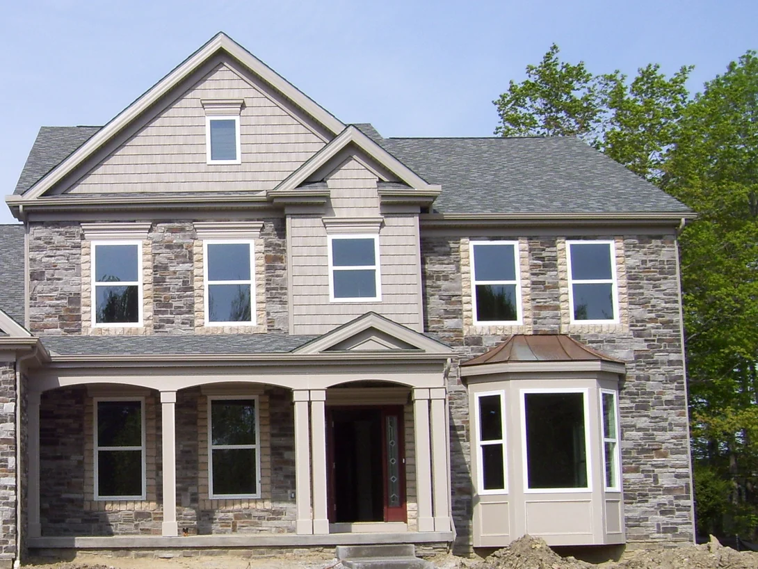 The front of a two-story manufactured stone house in May 2009, the surround and sill of every window a pale tan against grey and brown stone, with bare earth in front