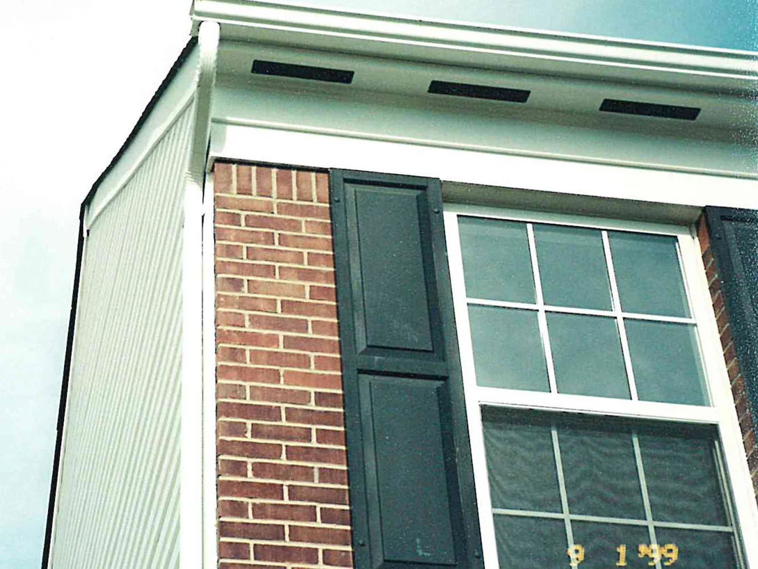 An upper corner of the house in 1999, brick running to a white soffit beside a sided return, the units reading unevenly light in places against a dark shutter