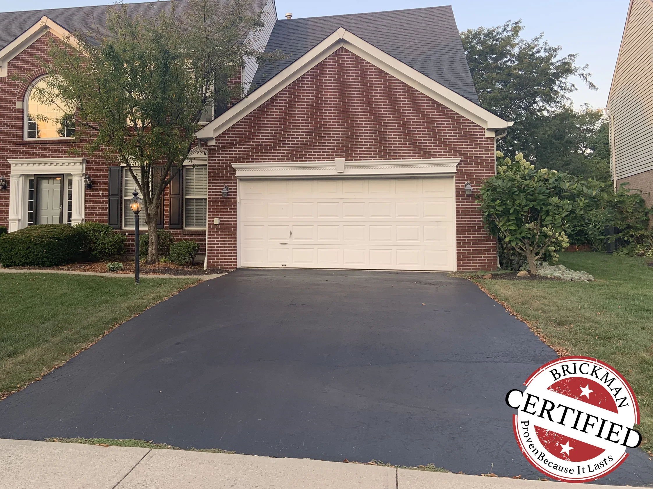 The front of the two-story brick home in 2019, gable-end garage beside a pedimented entry, the brick an even red range from the ground to the eaves