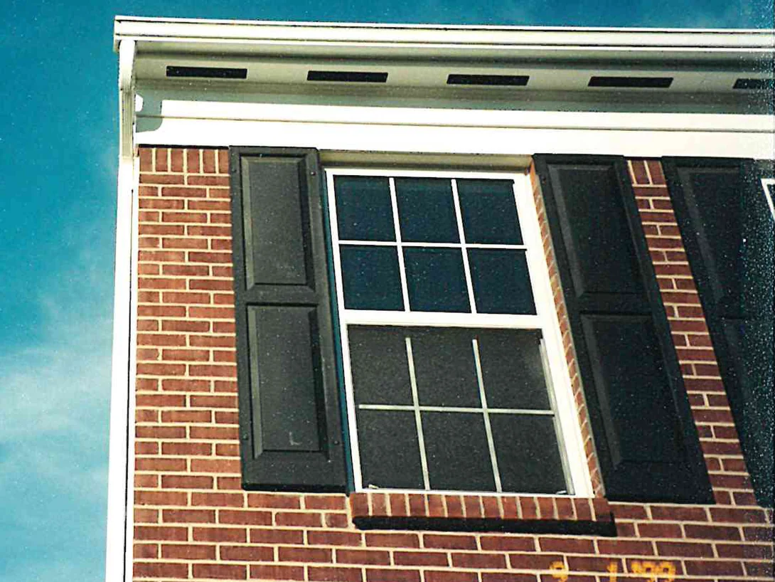 An upper wall of the house after staining in 1999, a white-trimmed window between dark shutters with the brick reading as one even red range