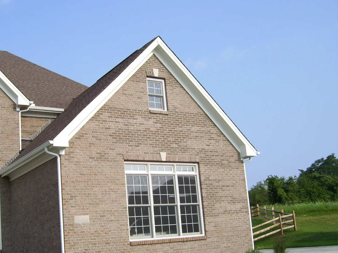 The gable end of the house in 2007 before staining, tan brick with a light uneven range around a tall white window, a split rail fence and open field beyond