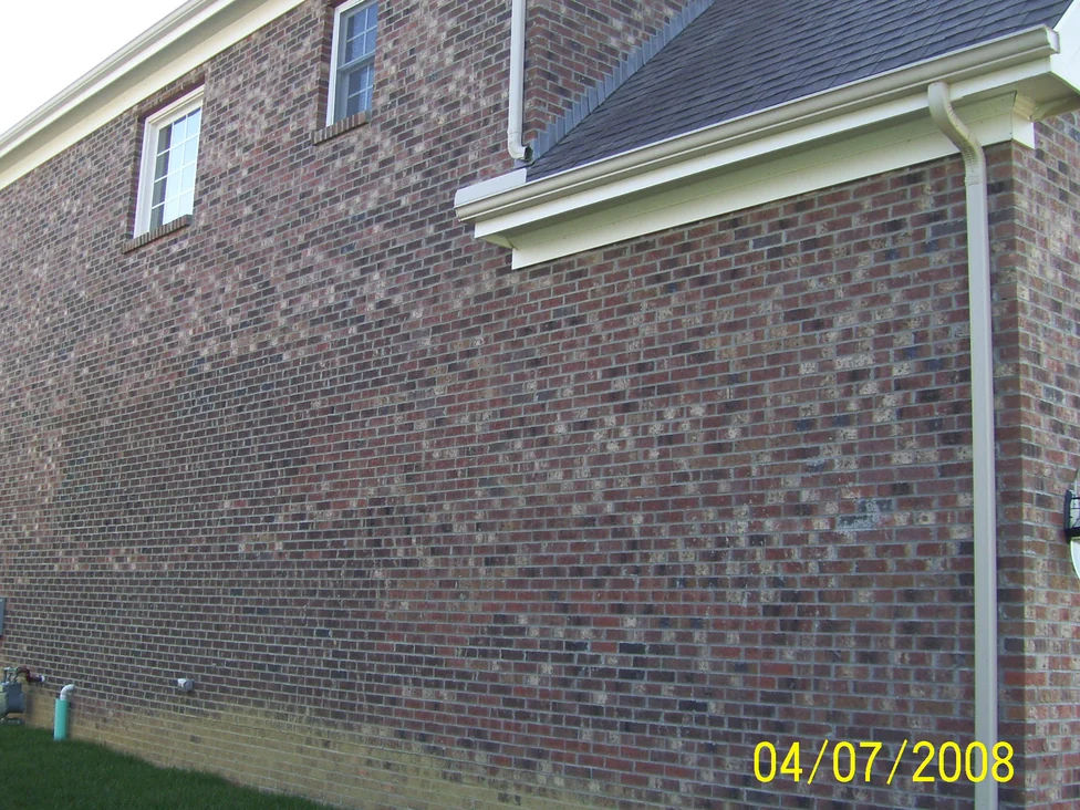 The long side wall of the house in 2008 before the work, dark and pale brick scattered unevenly through the range from the eaves down to the grass