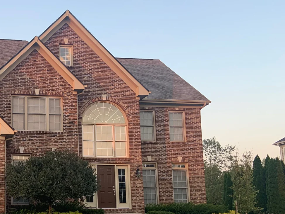 The front of the house in 2019, an arched entry window under a tall gable and a two-story wing beside it, the brick an even range of reds and browns from the eaves down to the planting.