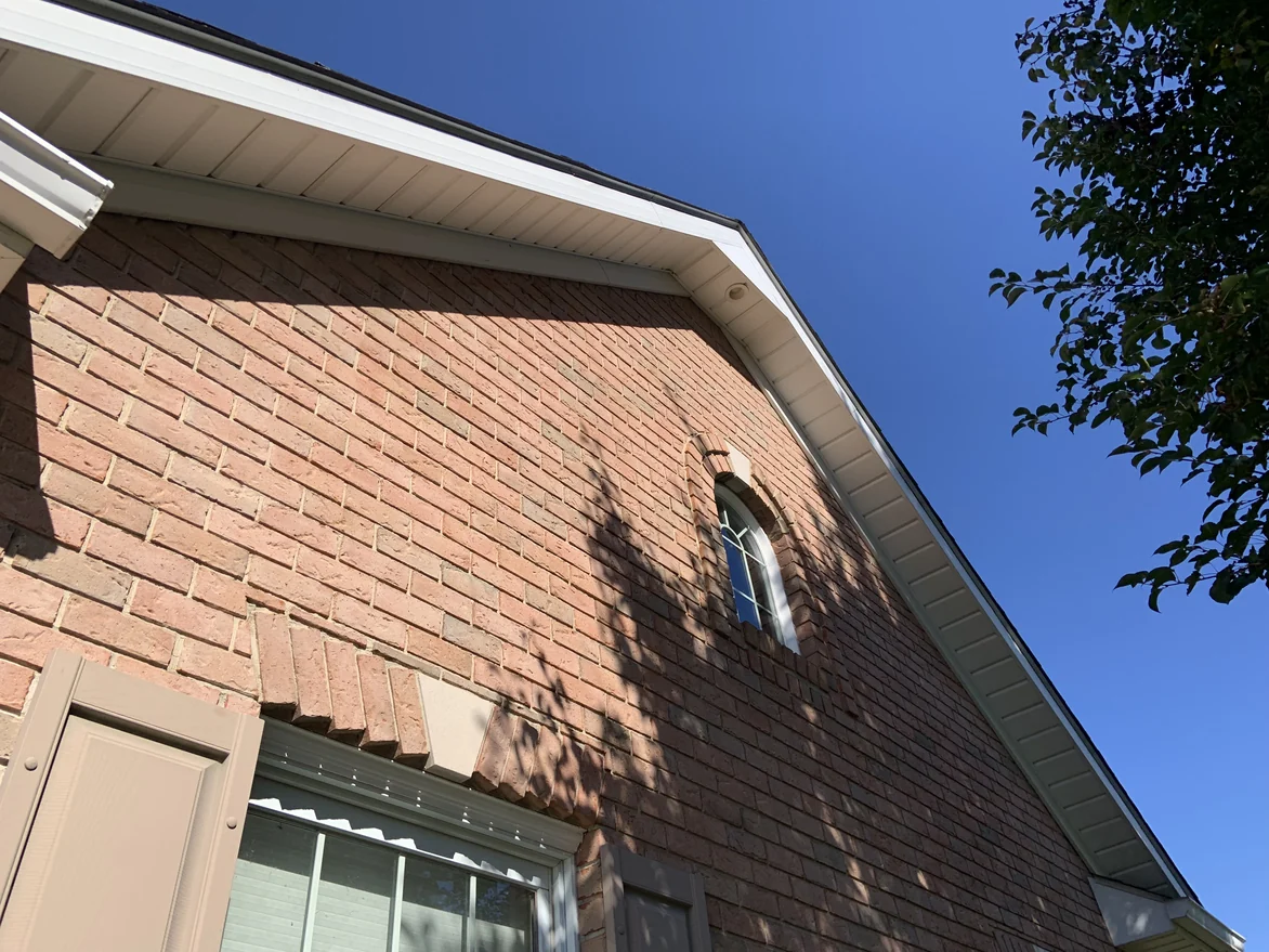 The gable wall of the house seen from below in 2019, the brick running unbroken up to the soffit and around the attic window