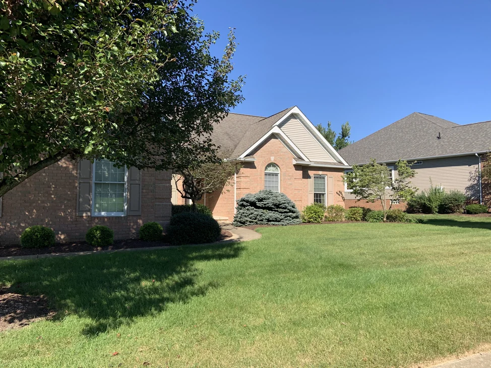 The single-story house from the front lawn in 2019, one red brick range running across the wall, the front gable and the entry.