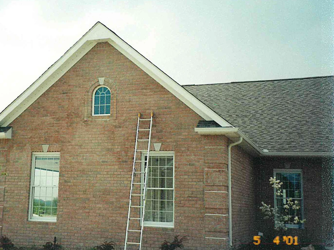 A ladder standing against the gable end of the house in 2001, the brick pale and patchy across the wall below the arched attic window