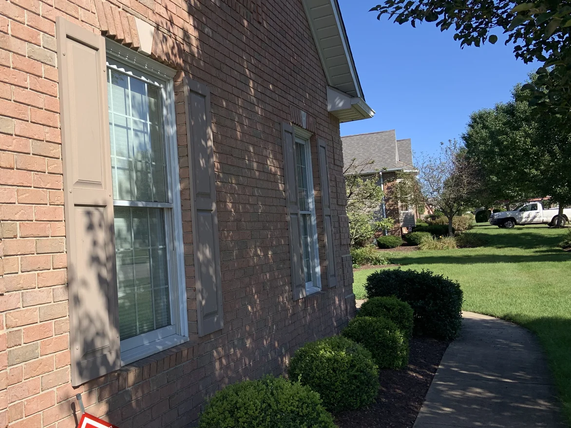 Two shuttered windows in the side wall of the house in 2019, the brick around and below them one consistent range