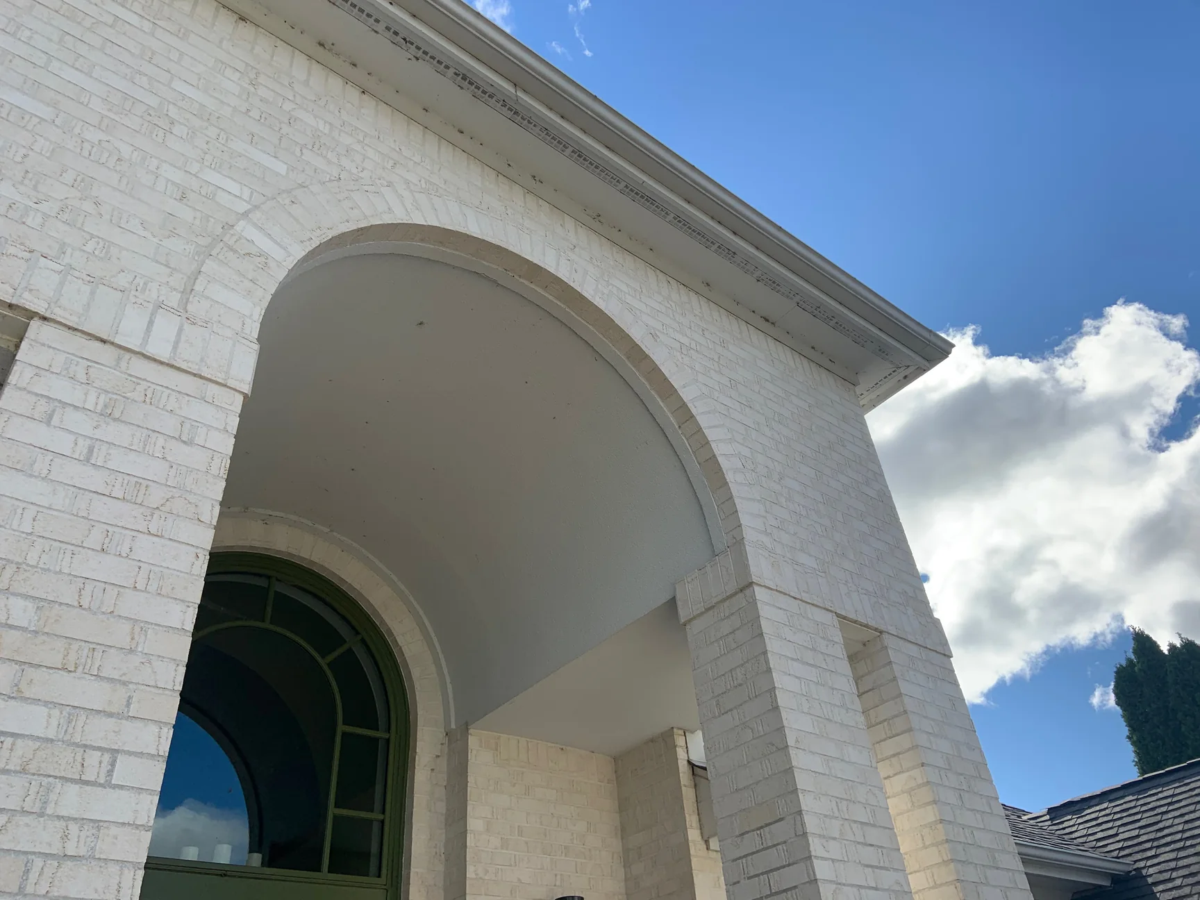 The arch of the entry portico in 2019 from close underneath, white brick voussoirs over the arched transom of the front door, the soffit and cornice above