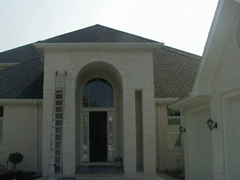 The arched entry of the white brick house in 2003, an extension ladder leaning on the left pier of the portico beside the front door