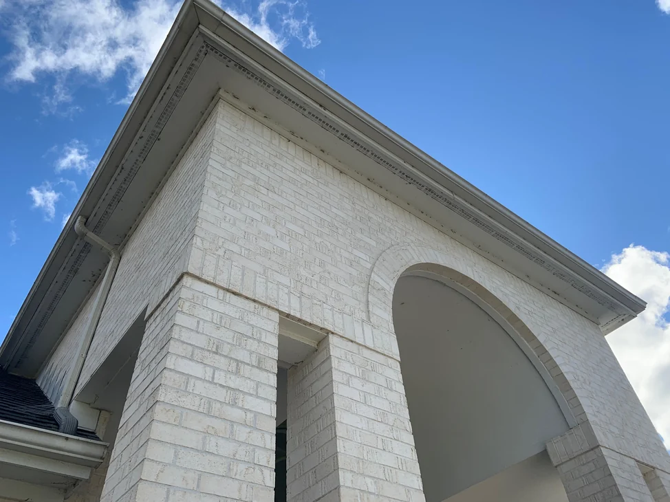 The entry portico of the Maumee house in 2019 looking up from the driveway, white brick piers and an arch under a dentil cornice, blue sky and cloud above.