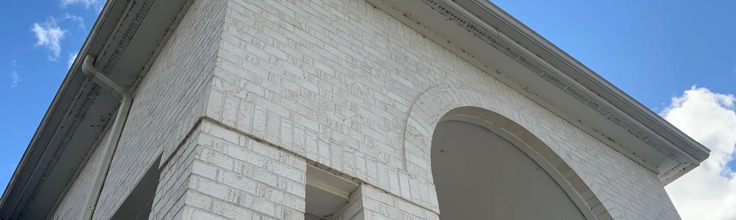The white brick entry portico of the Maumee house in 2019, seen from below against a blue sky, one arch and one square opening under a dentil cornice