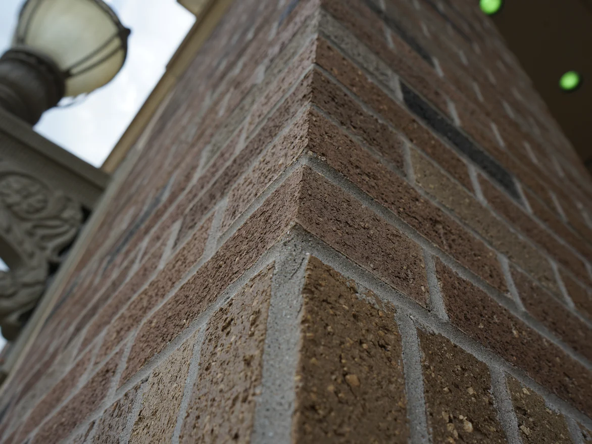 An outside brick corner at close range in 2019, the color sitting in the face of each unit with the fired speckle and the pitting still reading through it, mortar joints clean