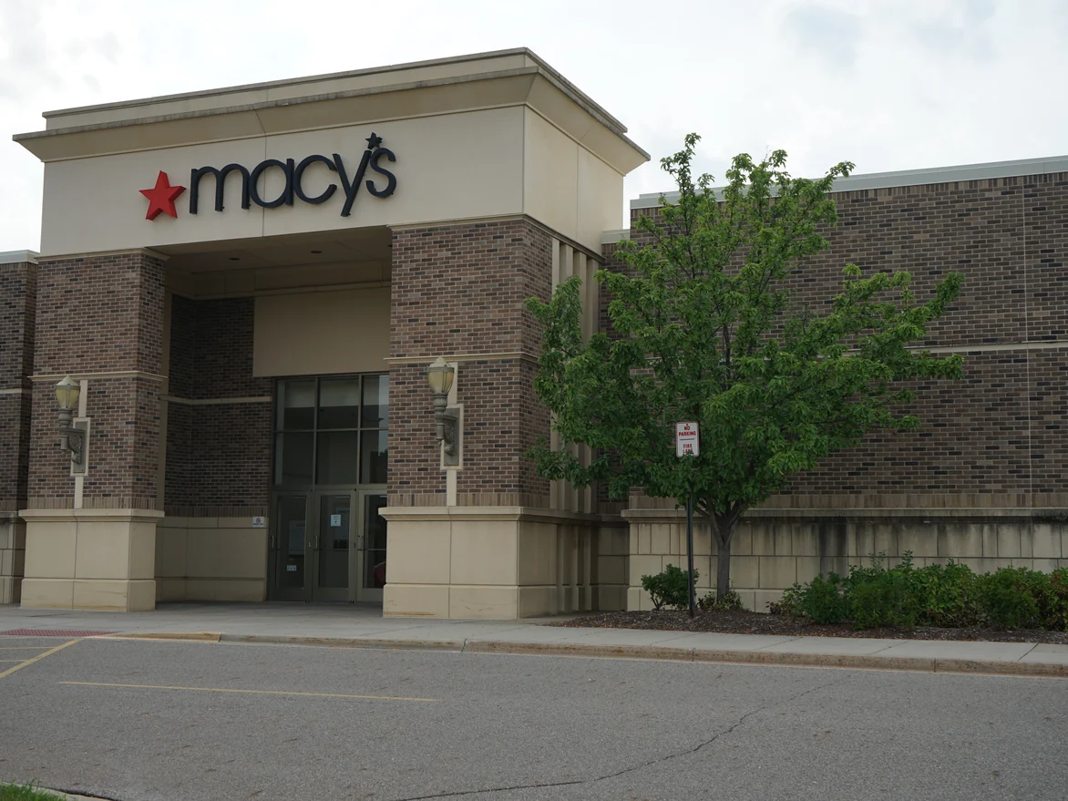 The anchor store entrance in 2019, the brick piers either side of the doors and the wall running away to the right holding the same brown and tan range under a cast stone cap