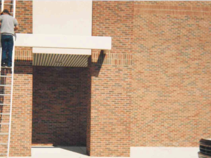 The entrance canopy in 1995 after staining, a man on an extension ladder at the left, the brick of the doorway now carrying the same flashed blend as the wall to the right