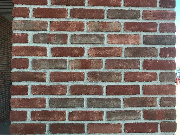 A close-up of the stained brick in 2019, red, brown and grey units with pale joints, several colors on a single brick