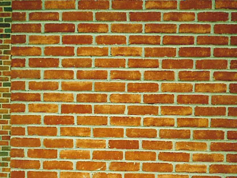 A close-up of the plain sand molded brick in 1995, every unit the same orange with pale grey joints, a sliver of the darker flashed blend at the left edge