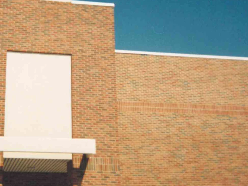 The entrance tower in 1995 after staining, its brick now carrying the same flashed blend as the wall to the right, under a deep blue sky