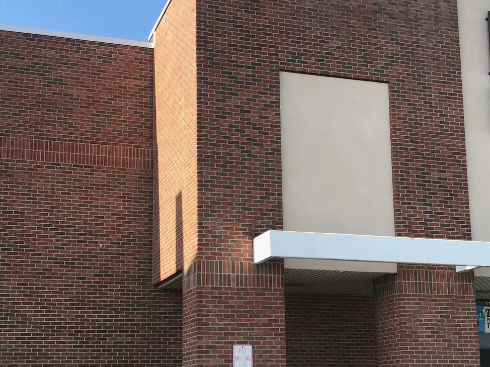The entrance tower and the wall beside it in 2019, one flashed red brown blend across both under a white canopy.