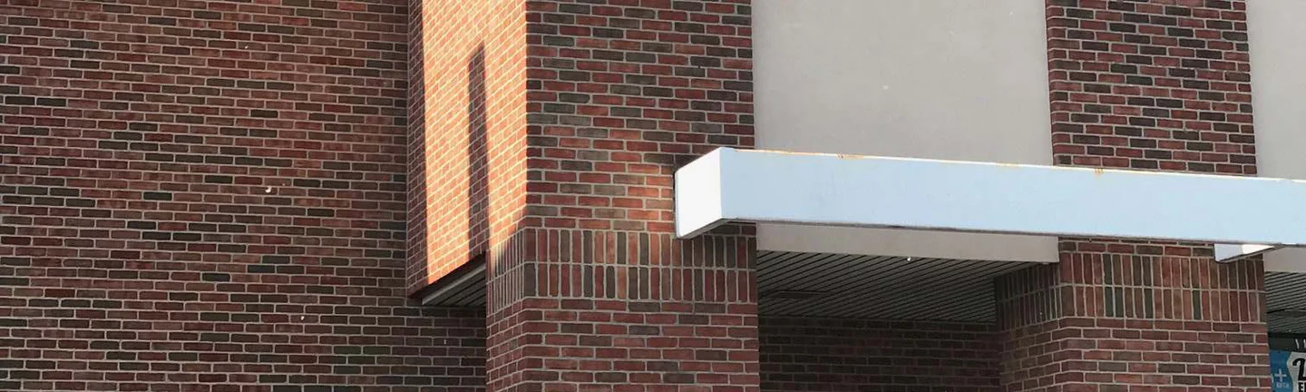 The entrance tower of the Merrillville retail building in 2019, its flashed red brown brick running under a white canopy into the wall beside it