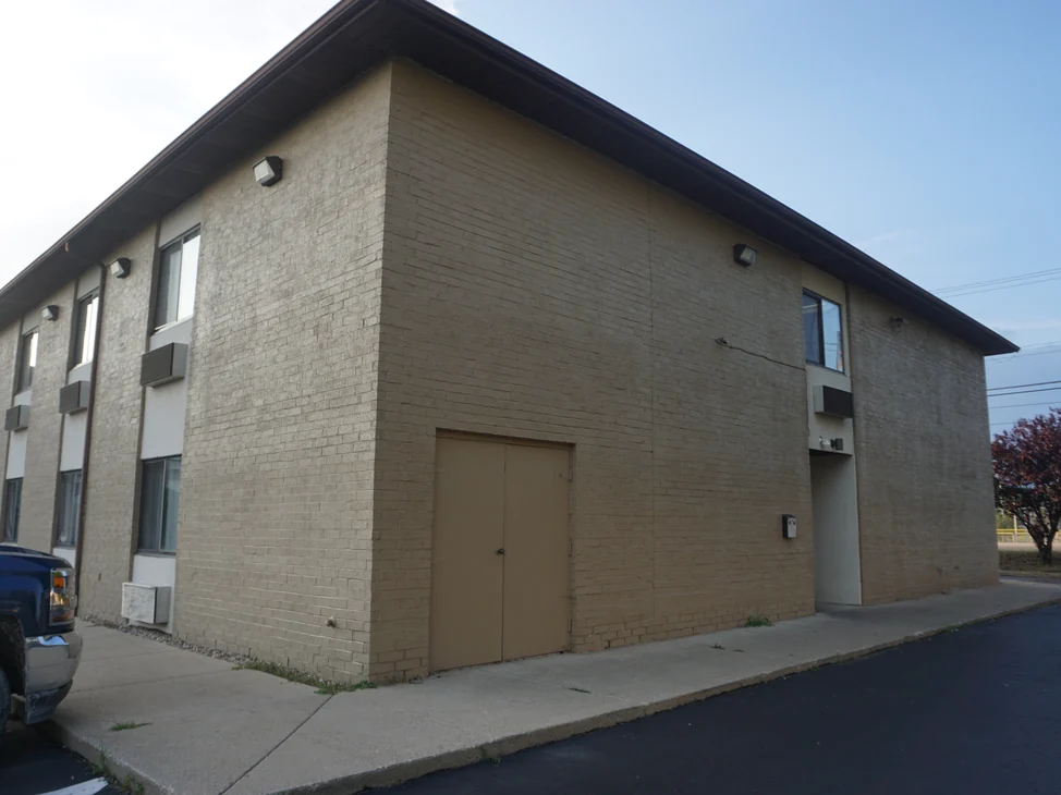 The corner of the Michigan hotel in 2019, both elevations under one flat coat of tan paint with the brick texture still showing through