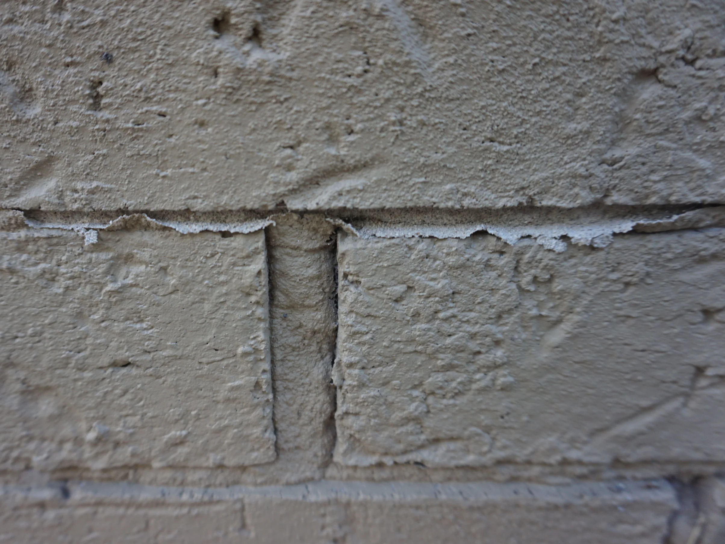 Close view of a bed joint in 2019, the coating broken away along the top edge of the brick below it and the joint opening beneath