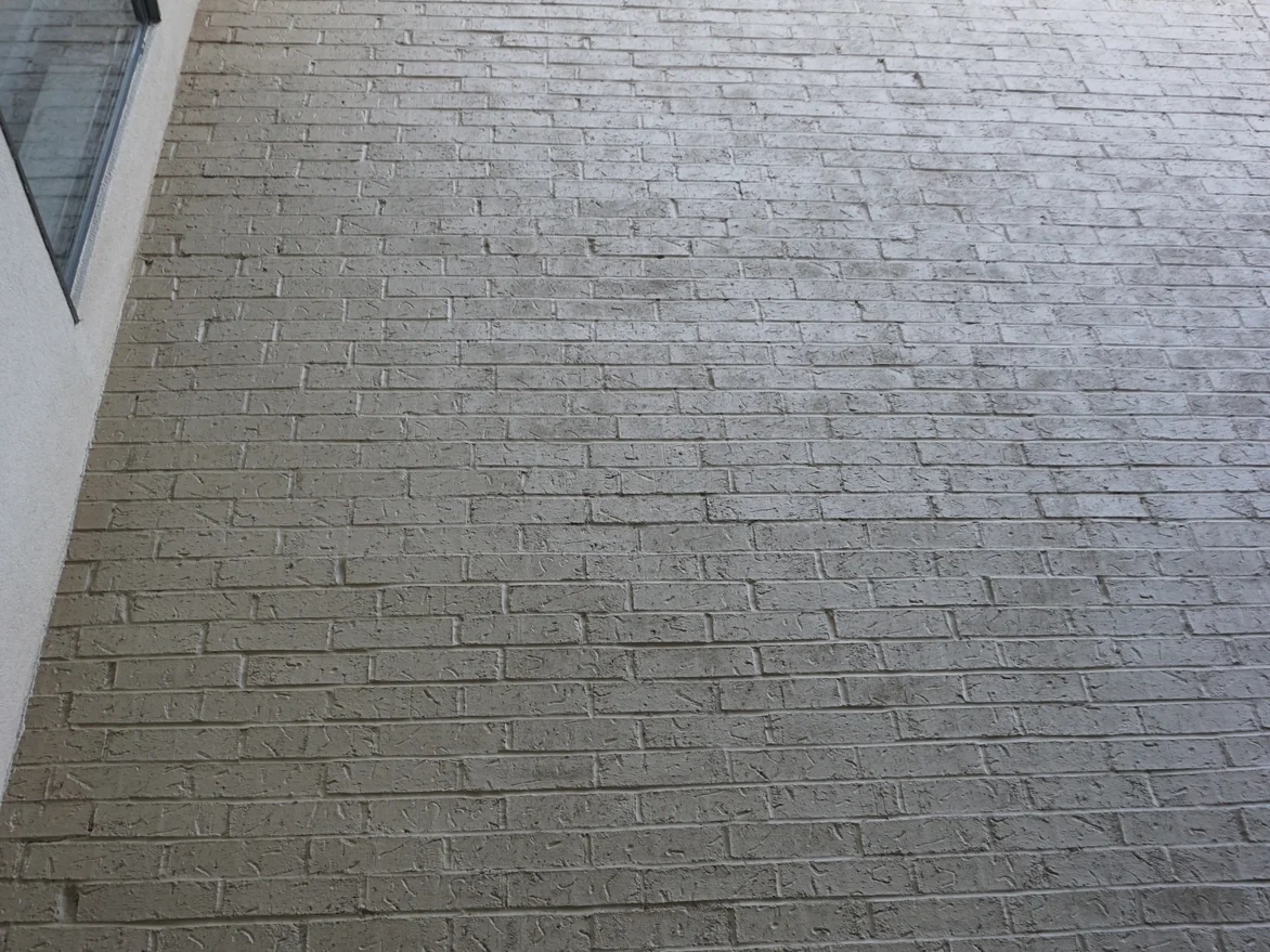 A two-story stretch of the hotel wall in 2019 seen from below, the coating flat tan and darkened by soiling toward the ground