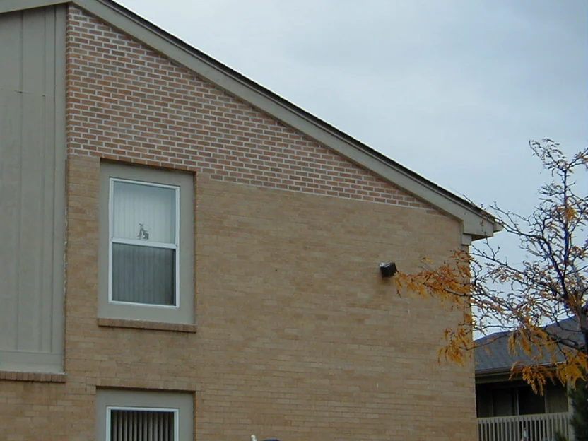 The gable end of the apartment block in 2000, a band of pink toned replacement brick running across the upper gable against the buff wall below it, with an applicator working at the foot of the frame