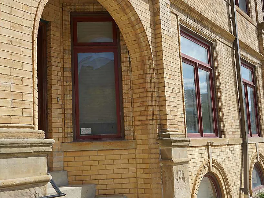 An arched entry in 2019 seen close, amber brick voussoirs over a tall arched window on a cast stone base, the wall beyond reading as one range to the next bay