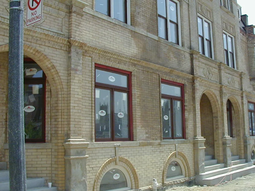The elevation in 2002, pale new brick at the base running up against darker older brick above, new windows still carrying maker stickers and bare dirt where the sidewalk was being rebuilt