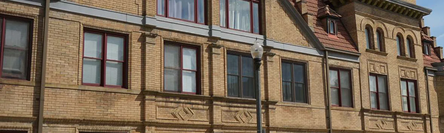 The street elevation in 2019, buff brick running past arched entries and a gabled bay under a red tile roof