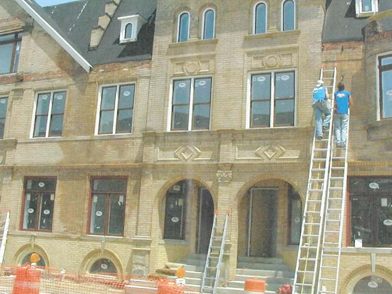 Two applicators on extension ladders working the upper wall in 2002, a third ladder against the storey below and orange safety fence along the sidewalk