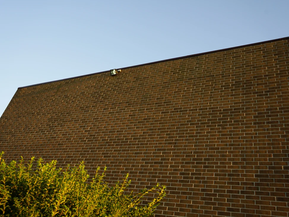 The end wall of the apartment block in 2019, its brick one even brown range from the parapet coping down to the ground.