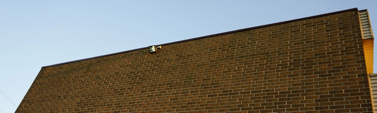 The end wall of the apartment block in 2019, its brick one even brown range under a dark parapet coping