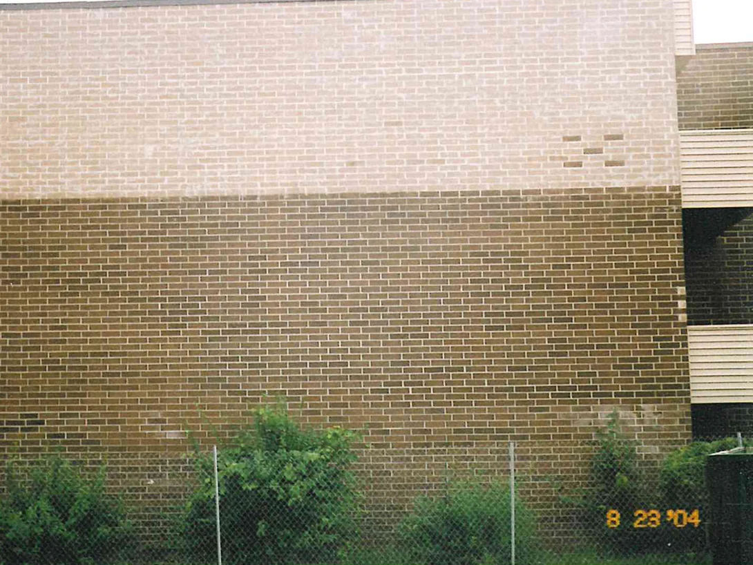 A pale band of newly laid brick running across the upper third of the wall, meeting the darker original brick below it in a hard horizontal line