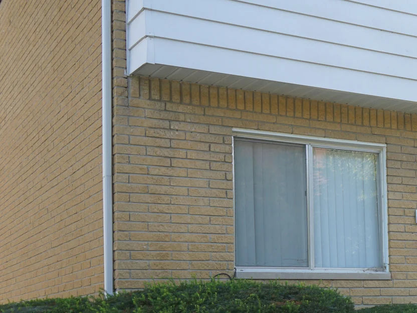 Close view of the buff brick at an outside corner in 2019, the courses running unbroken past a downpipe to a ground floor window with a soldier course above it