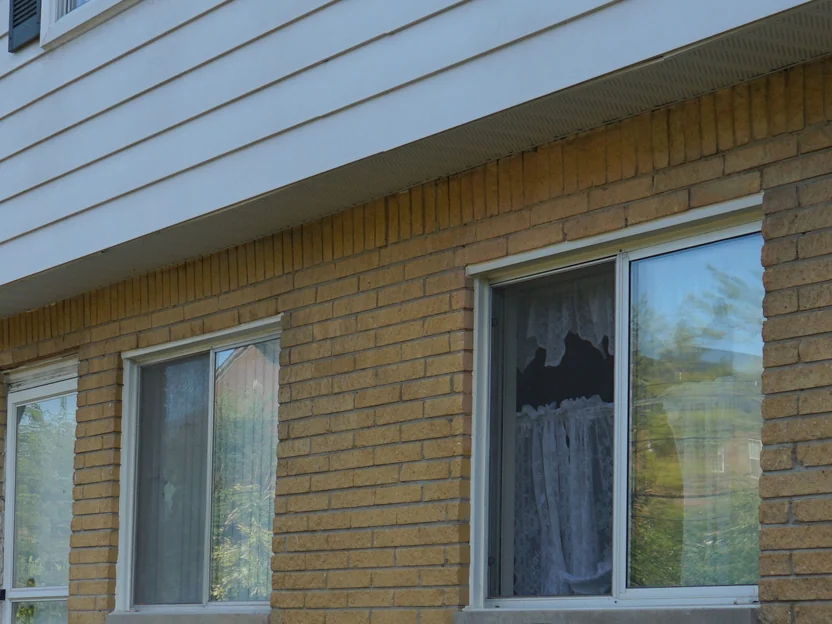 Three ground floor windows set in buff brick piers under the siding overhang in 2019, the brick one range across the piers and the header course