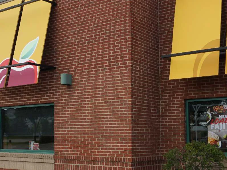 The same window bay in 2019, the striped awning replaced by yellow banners with the apple mark, the brick around it one even red range