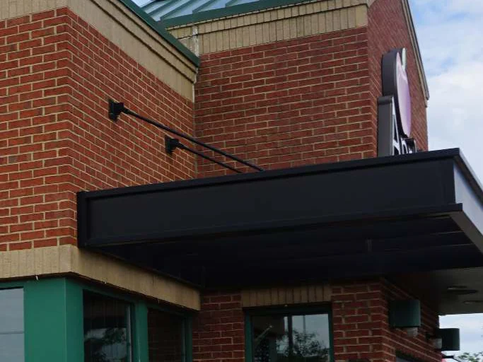 The canopy corner in 2019, red brick above a black steel canopy with a lamp arm, green window frames below and the edge of the sign at the right