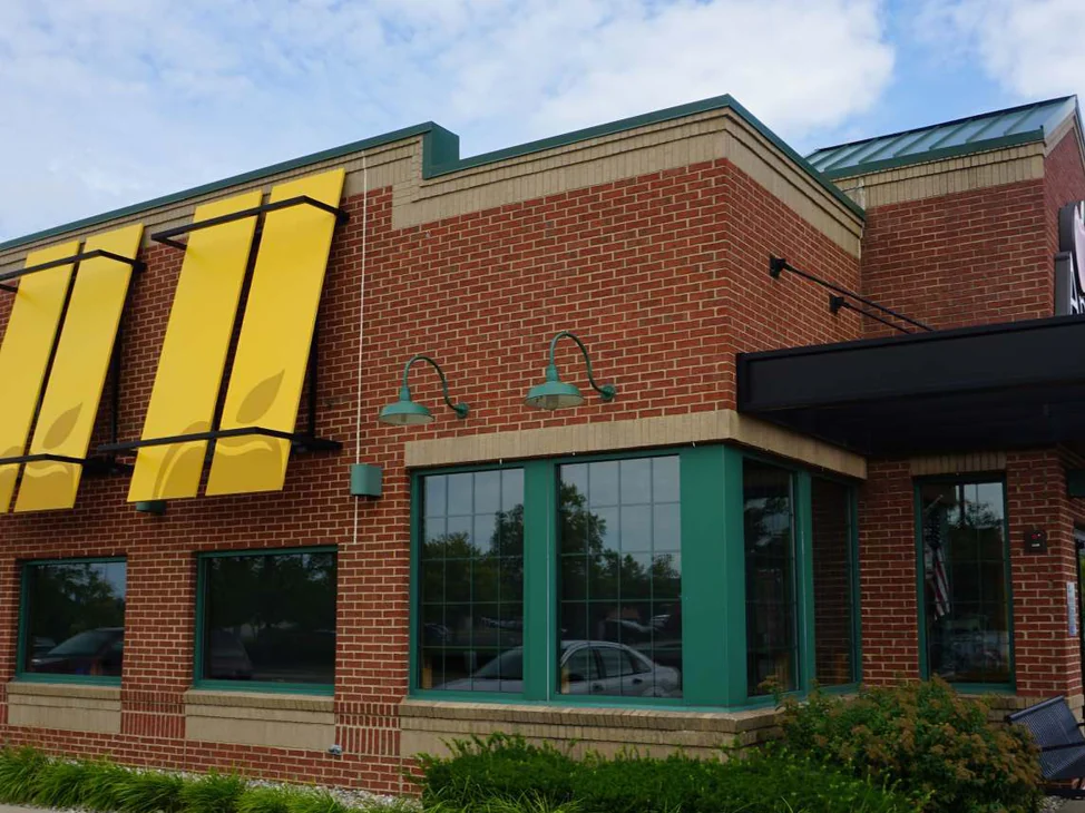 The front corner of the Michigan restaurant in 2019, red brick with buff bands under yellow awnings and green gooseneck lamps