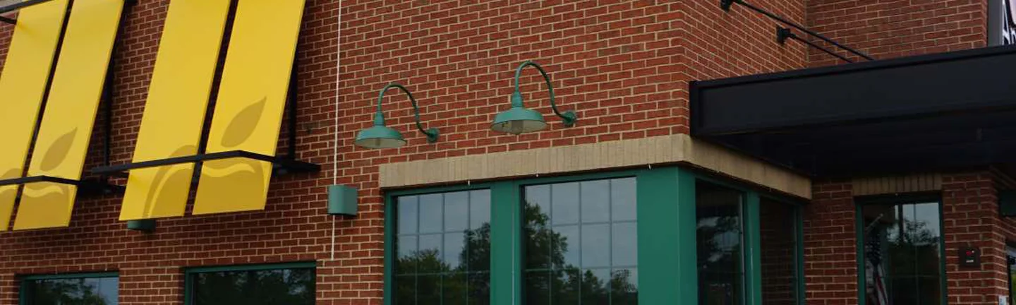 The front corner of the Michigan restaurant in 2019, red brick with buff bands under yellow awnings and green gooseneck lamps